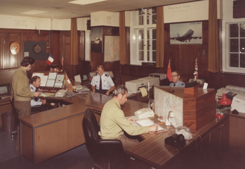 Five officers in uniform sit at desks in an office.