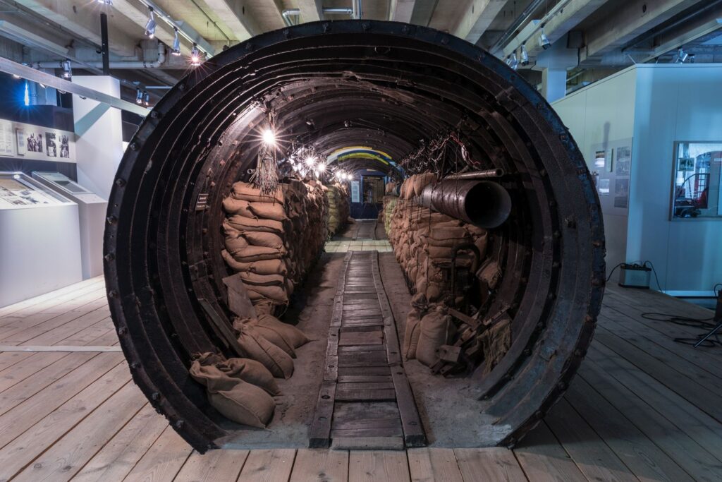 Vue sur l’intérieur du tunnel d’espionnage composé d’un tuyau en métal avec, sur les deux côtés, des sacs de sable, des câbles et, au centre, une rangée d’ampoules et un passage