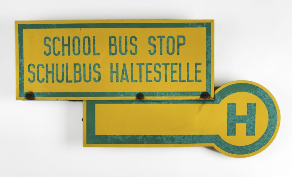 Panneau jaune et vert indiquant : School Bus Stop – Schulbus Haltestelle [Arrêt bus scolaire]