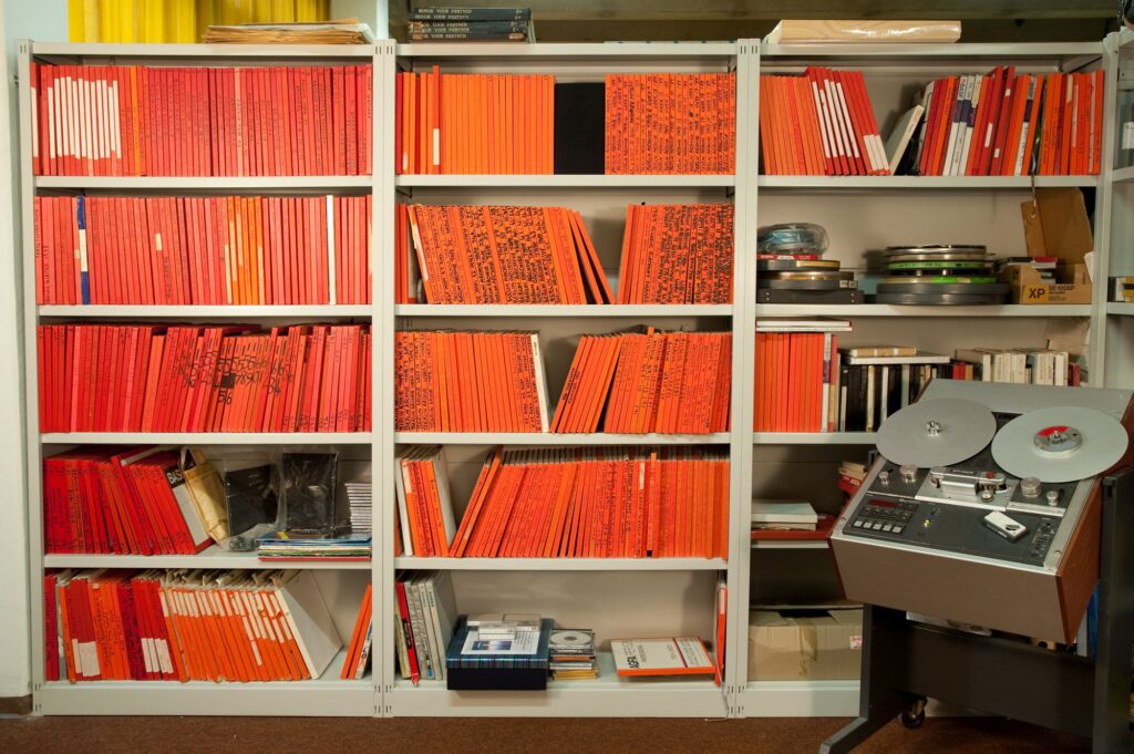 Shelf with audio tapes in orange storage containers and a tape recorder to the right 