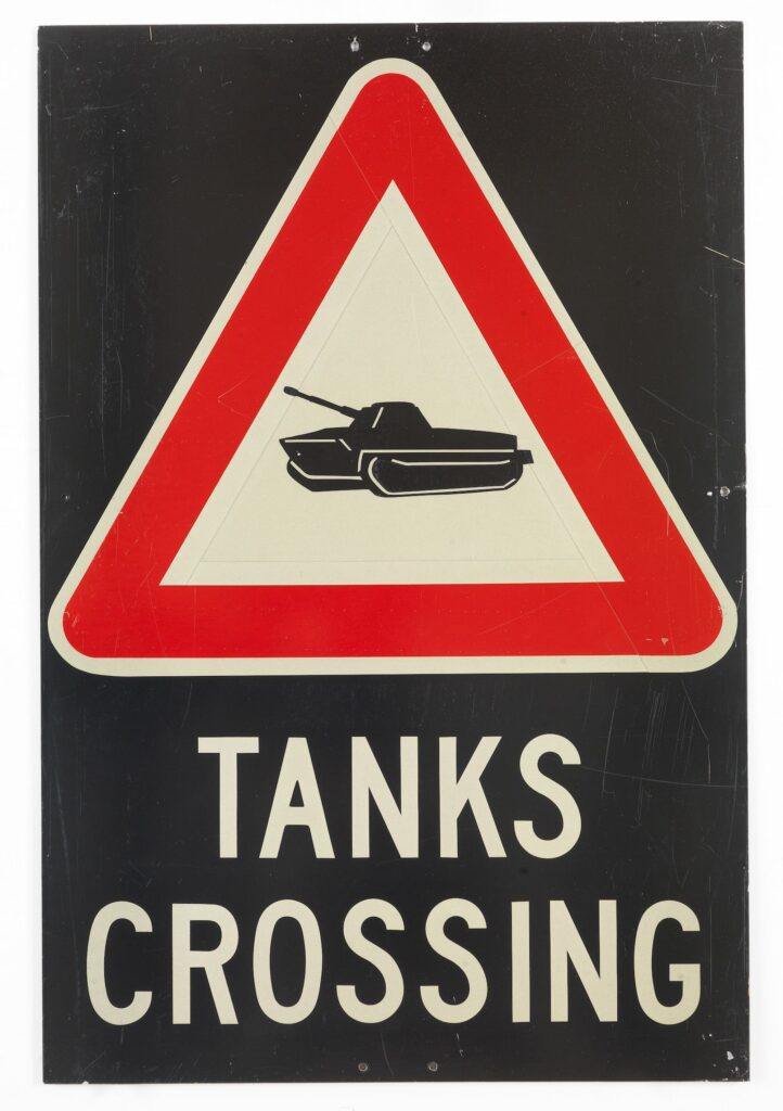 Panneau de signalisation triangulaire avec un char et le texte « Tanks Crossing »