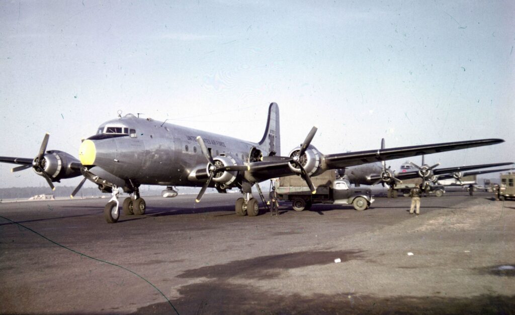 Flugzeuge der US Air Force vom Typ C-54 stehen aufgereiht hintereinander und werden mit LKWs entladen.